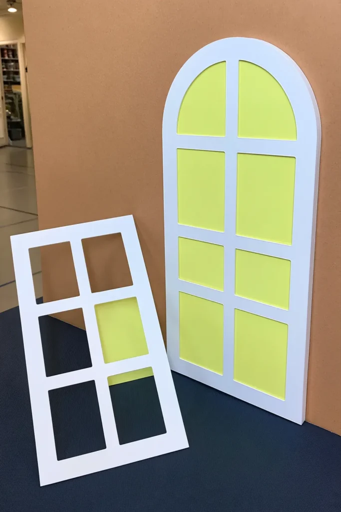 DIY gingerbread house window decorations with bright yellow panels, white rectangular window grids, and an arched white frame.
